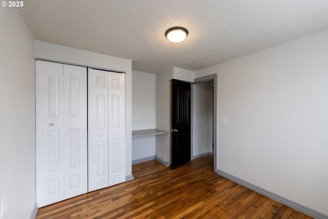 unfurnished bedroom featuring a textured ceiling, dark wood-type flooring, a closet, and baseboards