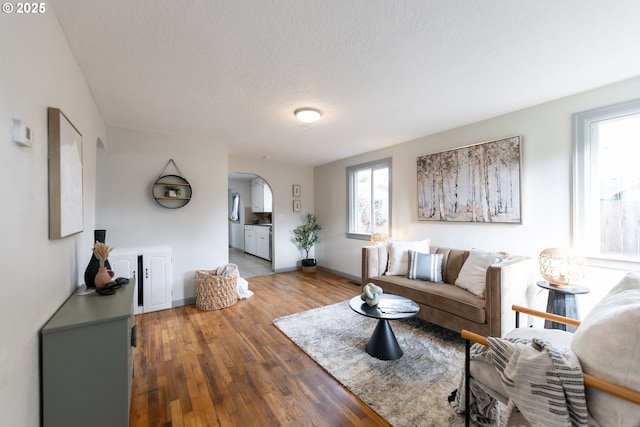 living room with arched walkways, a textured ceiling, wood finished floors, and baseboards