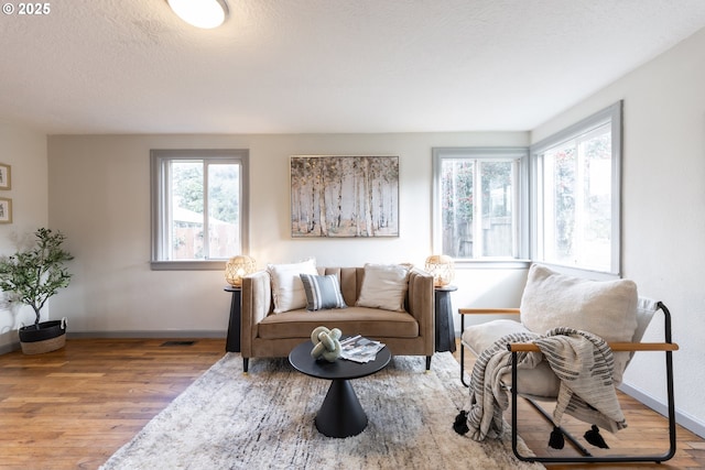 living area with a textured ceiling, wood finished floors, visible vents, and baseboards