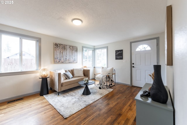 living room with visible vents, a textured ceiling, baseboards, and wood finished floors