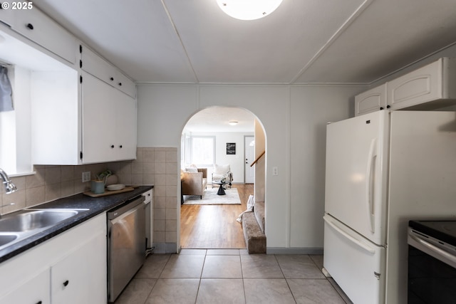 kitchen with light tile patterned floors, arched walkways, dark countertops, stainless steel dishwasher, and a sink