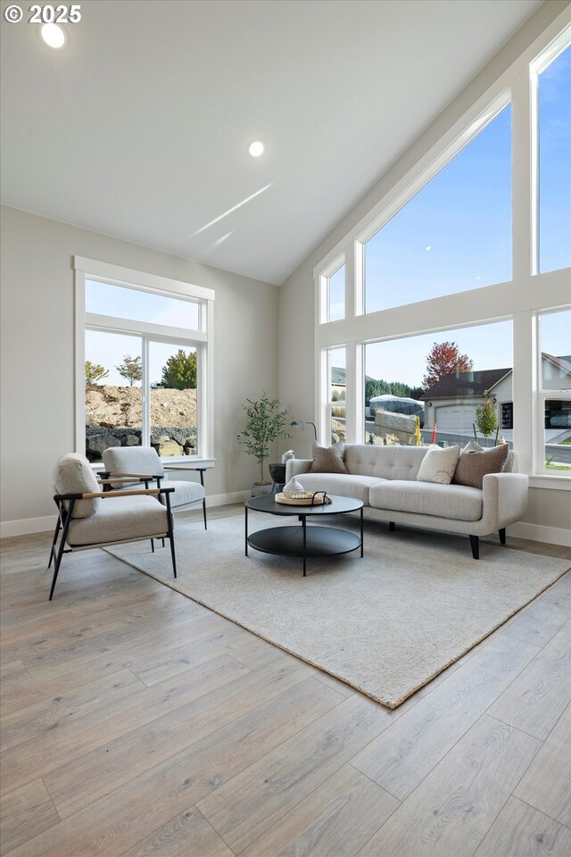 living room with plenty of natural light, high vaulted ceiling, and light hardwood / wood-style flooring