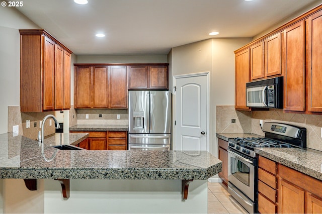 kitchen with a breakfast bar, a sink, stainless steel appliances, a peninsula, and light tile patterned floors