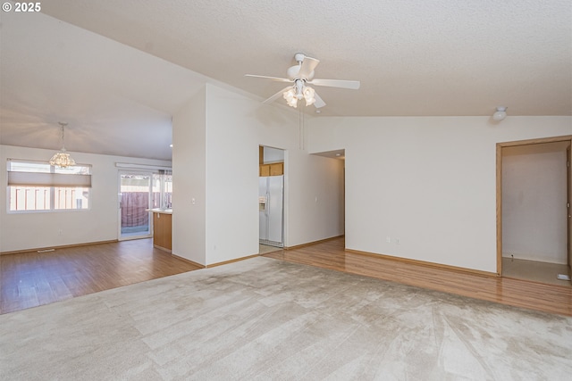 carpeted empty room with a ceiling fan, vaulted ceiling, a textured ceiling, and wood finished floors