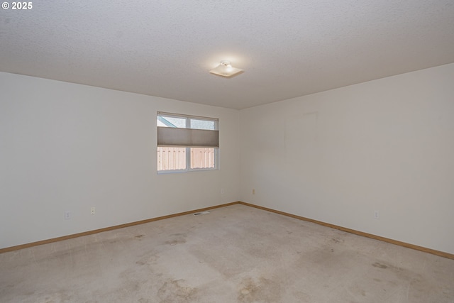 spare room featuring a textured ceiling, light carpet, visible vents, and baseboards