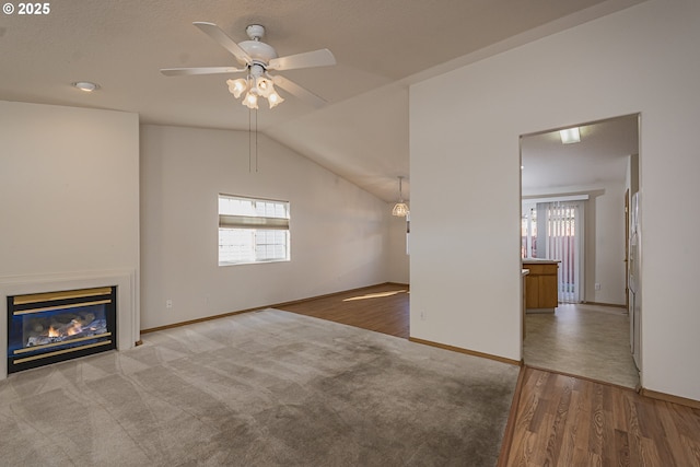 unfurnished living room featuring a glass covered fireplace, vaulted ceiling, baseboards, and wood finished floors