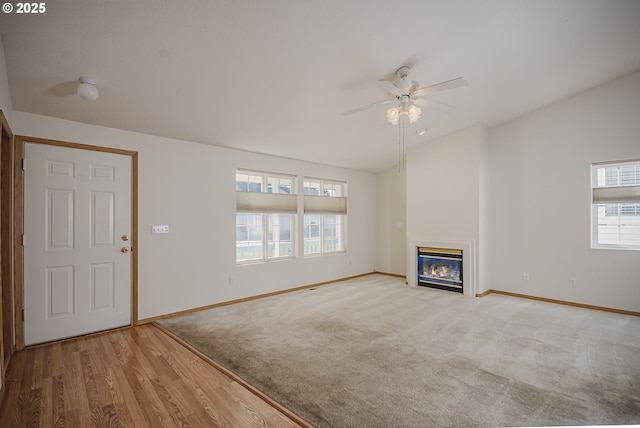 unfurnished living room featuring baseboards, vaulted ceiling, a wealth of natural light, and a glass covered fireplace