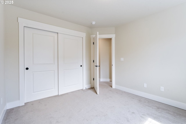 unfurnished bedroom with baseboards, light carpet, and a closet