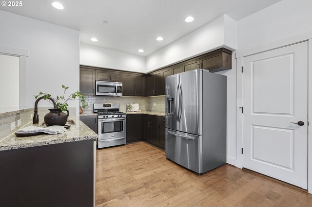 kitchen with dark brown cabinetry, appliances with stainless steel finishes, light wood-style floors, and light stone counters