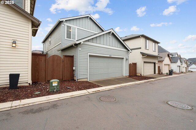 view of front of home featuring board and batten siding, a gate, fence, a garage, and a residential view