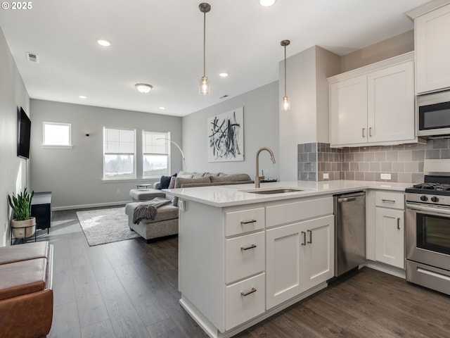 kitchen featuring appliances with stainless steel finishes, kitchen peninsula, white cabinets, decorative light fixtures, and sink