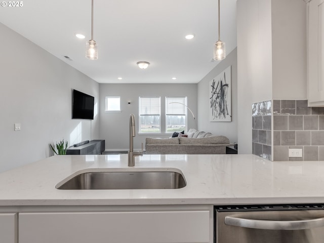 kitchen with light stone countertops, stainless steel dishwasher, hanging light fixtures, white cabinets, and sink