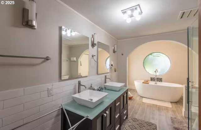 bathroom featuring a washtub, hardwood / wood-style flooring, crown molding, tile walls, and vanity