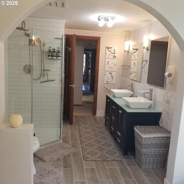 bathroom with vanity, toilet, a shower with door, and tile walls