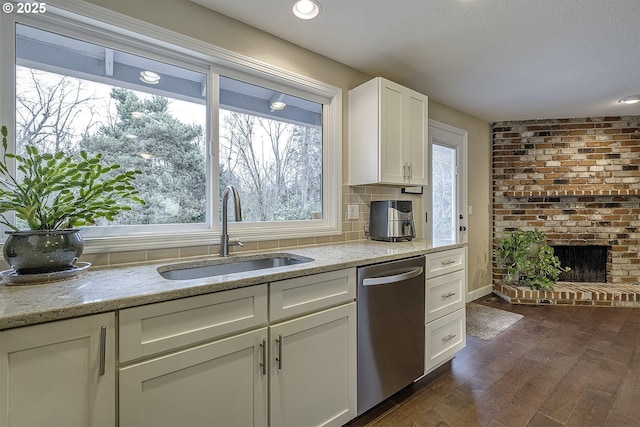 kitchen featuring a sink, stainless steel dishwasher, dark wood finished floors, white cabinets, and a brick fireplace