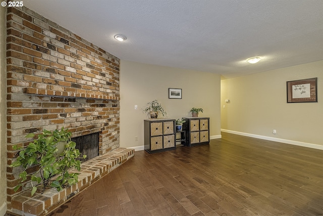 living room featuring a brick fireplace, a textured ceiling, baseboards, and wood finished floors