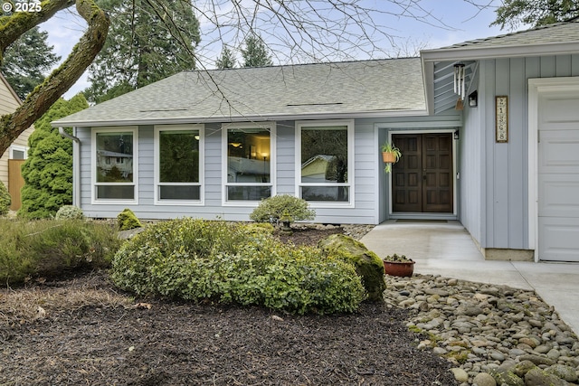 doorway to property with roof with shingles, board and batten siding, and an attached garage