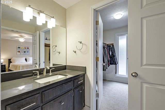 ensuite bathroom with connected bathroom, ceiling fan, vanity, a textured wall, and a textured ceiling