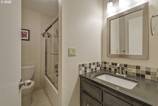 bathroom featuring vanity, shower / bath combination with glass door, toilet, a textured wall, and backsplash