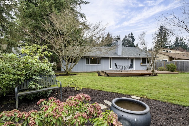 rear view of property with a lawn, a deck, a chimney, and fence