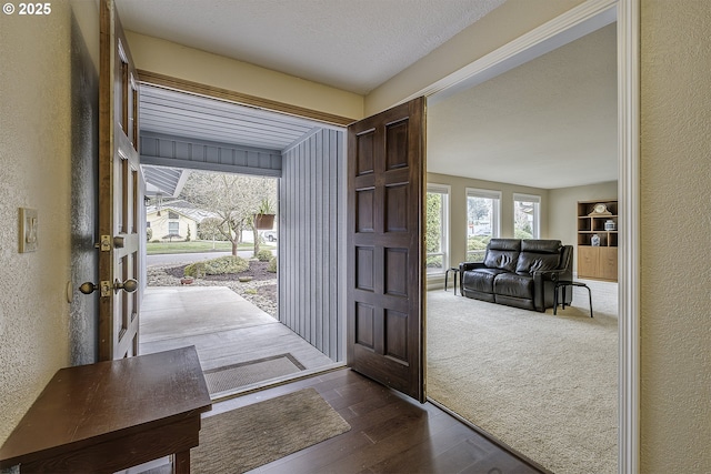 entrance foyer featuring dark wood-style flooring, dark carpet, a textured ceiling, and a textured wall