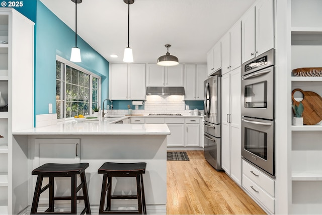 kitchen featuring appliances with stainless steel finishes, sink, white cabinets, a kitchen breakfast bar, and kitchen peninsula