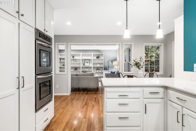 kitchen with white cabinetry, double oven, decorative light fixtures, kitchen peninsula, and light wood-type flooring