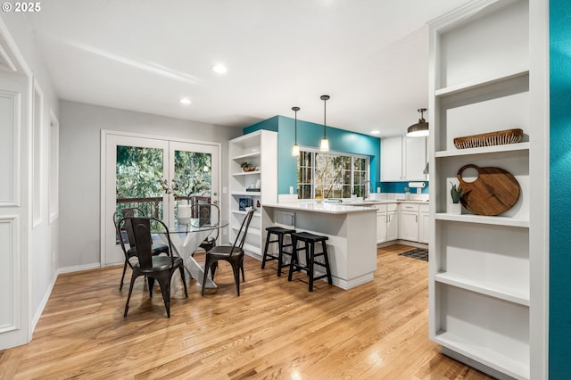 kitchen featuring a breakfast bar, decorative light fixtures, white cabinetry, kitchen peninsula, and light hardwood / wood-style flooring