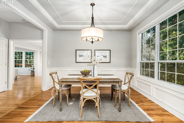 dining space with a raised ceiling, a wealth of natural light, and light hardwood / wood-style flooring