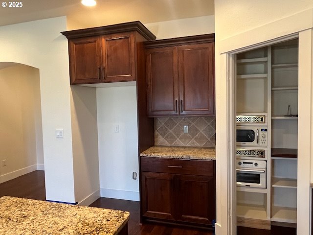 101 Rome St, Boardman, OR 97818 - kitchen with dark wood-style flooring, arched walkways, tasteful backsplash, baseboards, and light stone counters