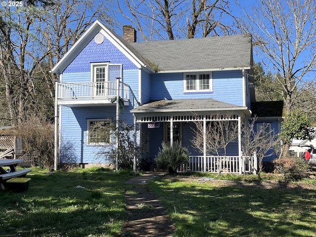 victorian home featuring a chimney, a balcony, covered porch, and a front lawn