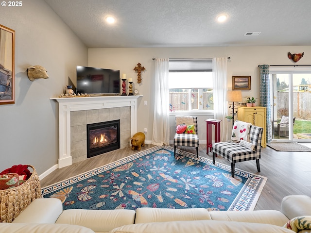 living room featuring a tile fireplace, wood-type flooring, and a textured ceiling