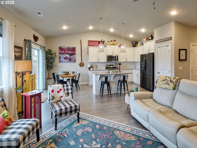 living room featuring lofted ceiling, sink, and light hardwood / wood-style flooring