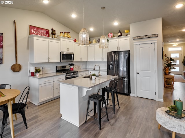 kitchen featuring appliances with stainless steel finishes, white cabinetry, sink, hanging light fixtures, and a kitchen island with sink