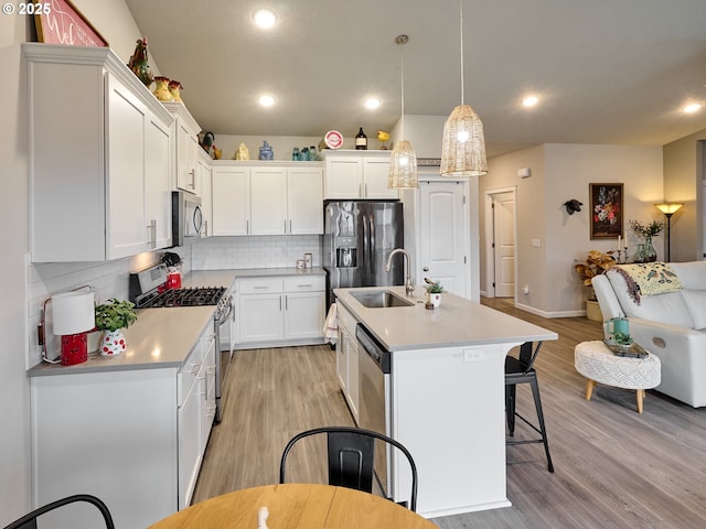 kitchen featuring white cabinetry, light hardwood / wood-style flooring, hanging light fixtures, a center island with sink, and appliances with stainless steel finishes