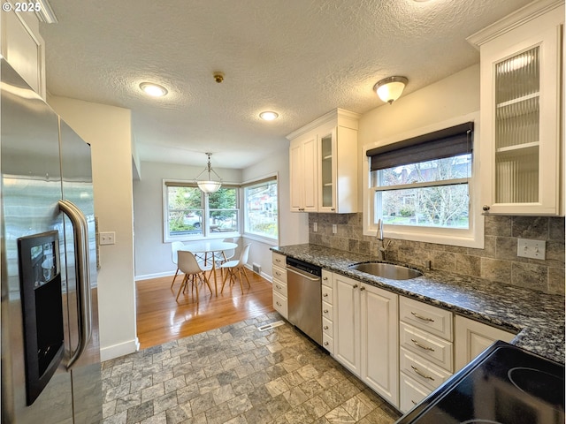 kitchen with baseboards, a sink, decorative backsplash, stainless steel appliances, and glass insert cabinets