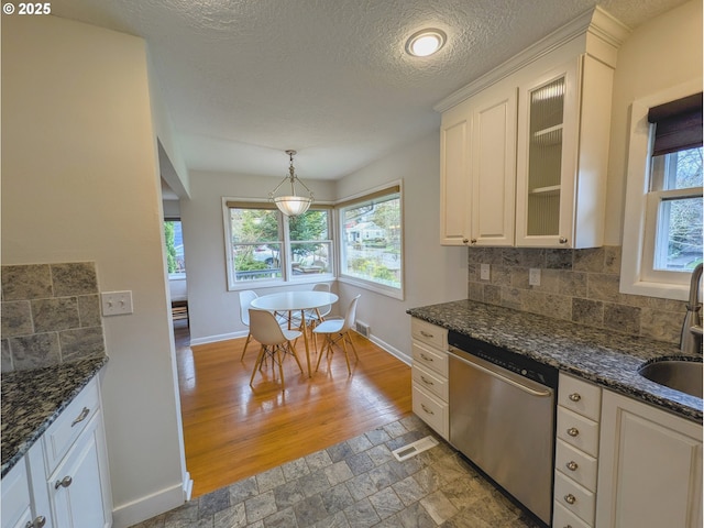 kitchen featuring baseboards, glass insert cabinets, stone finish flooring, stainless steel dishwasher, and backsplash