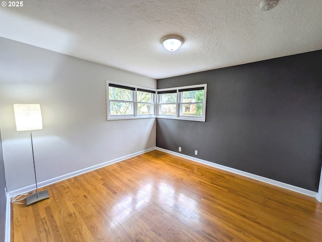 empty room with baseboards, a textured ceiling, and wood finished floors