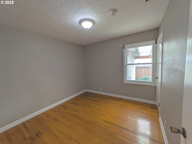 empty room featuring a textured ceiling, baseboards, and wood finished floors