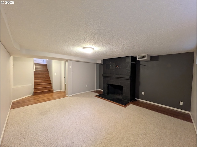 unfurnished living room featuring a textured ceiling, wood finished floors, stairway, a fireplace, and baseboards