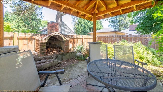 view of patio with a fenced backyard, outdoor dining space, and an outdoor brick fireplace