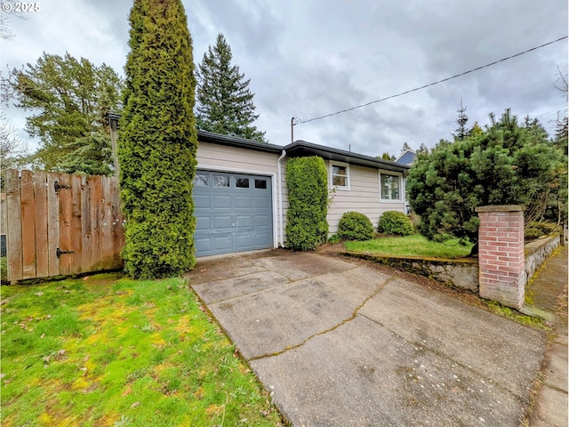 view of front of property featuring an attached garage, concrete driveway, a front lawn, and fence