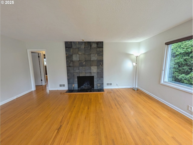 unfurnished living room featuring visible vents, baseboards, a tile fireplace, wood finished floors, and a textured ceiling