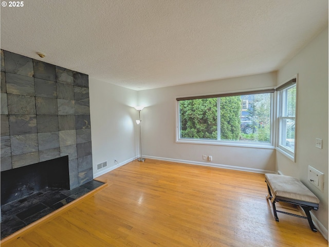 unfurnished living room featuring visible vents, plenty of natural light, a textured ceiling, and wood finished floors