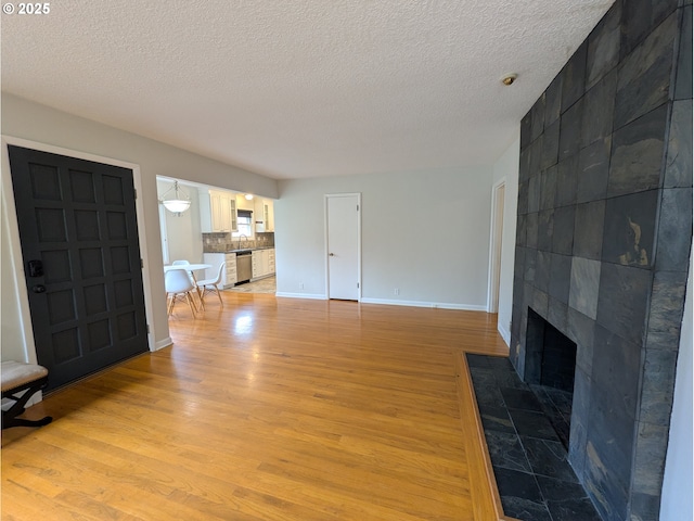 living area featuring a fireplace, baseboards, light wood finished floors, and a textured ceiling