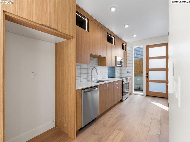 kitchen with sink, light wood-type flooring, appliances with stainless steel finishes, tasteful backsplash, and a healthy amount of sunlight