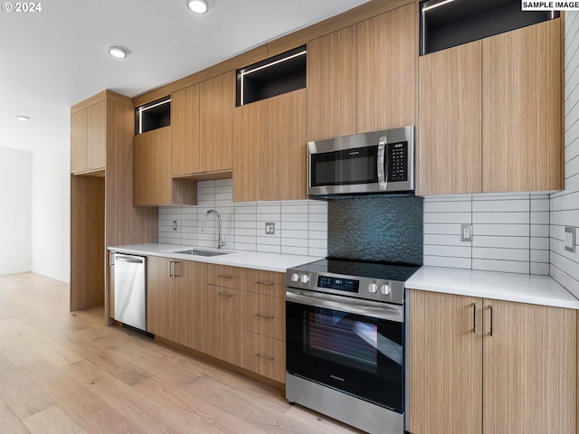 kitchen with appliances with stainless steel finishes, backsplash, light hardwood / wood-style flooring, and sink