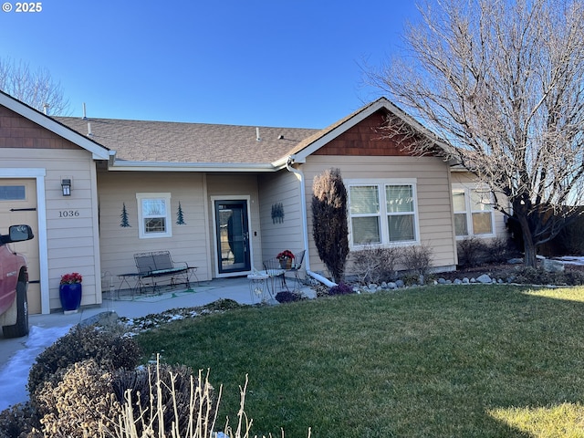 view of front facade featuring a front lawn, roof with shingles, and a patio