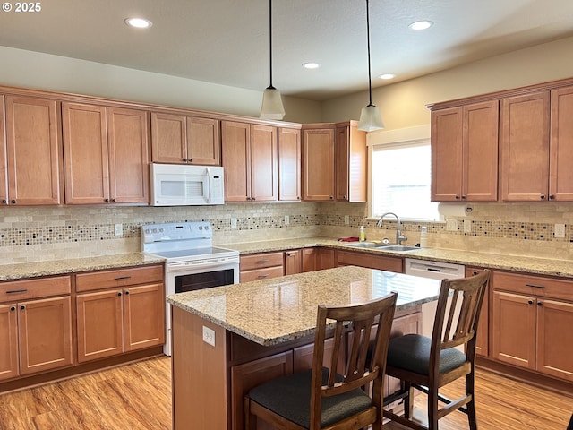 kitchen featuring white appliances, a sink, a breakfast bar area, light wood-style flooring, and pendant lighting