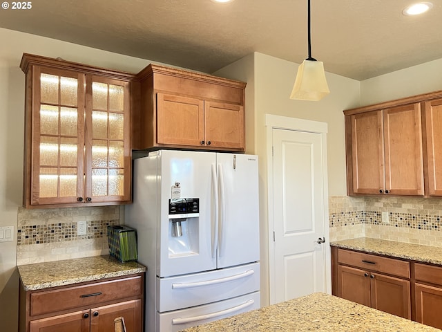 kitchen featuring white refrigerator with ice dispenser, pendant lighting, backsplash, and light stone counters